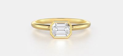 An east west bezel setting in yellow gold featuring an emerald lab grown diamond