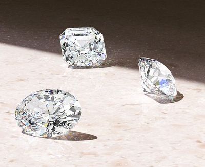 A round diamond, Asscher diamond and oval diamond on a table.